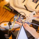Equipe trabalha em conjunto em um projeto de Arduino, com fios e placa de prototipagem sobre a mesa.