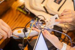 Equipe trabalha em conjunto em um projeto de Arduino, com fios e placa de prototipagem sobre a mesa.