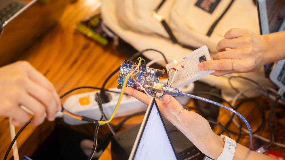 Equipe trabalha em conjunto em um projeto de Arduino, com fios e placa de prototipagem sobre a mesa.