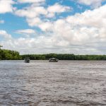 Embarcações navegam por um rio cercado por vegetação no Maranhão, sob céu claro.