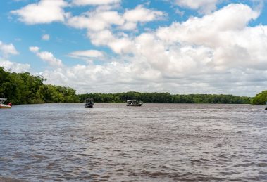 Embarcações navegam por um rio cercado por vegetação no Maranhão, sob céu claro.