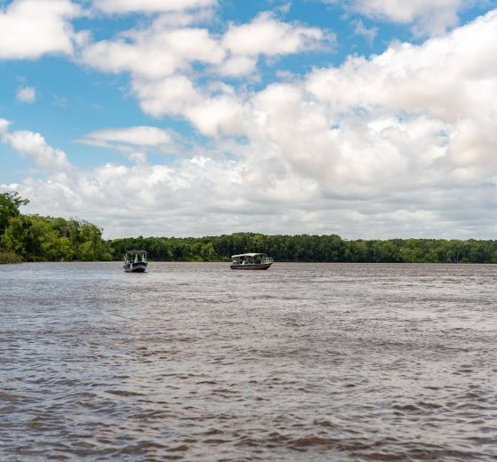 Embarcações navegam por um rio cercado por vegetação no Maranhão, sob céu claro.
