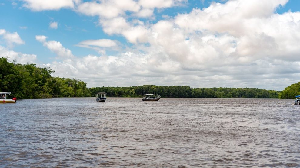 Embarcações navegam por um rio cercado por vegetação no Maranhão, sob céu claro.