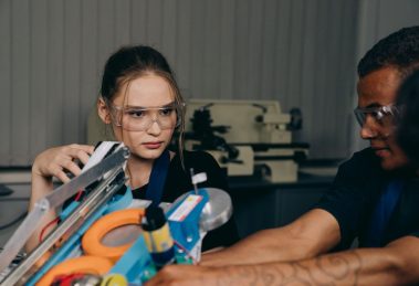 Jovens engenheiros colaboram na montagem de um equipamento robótico em uma oficina industrial.