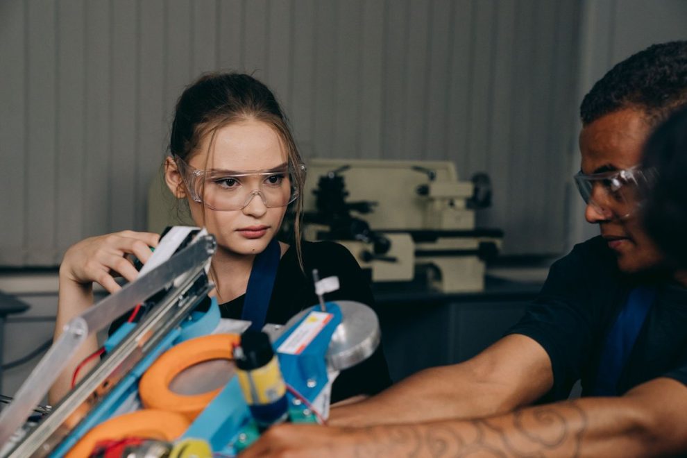 Jovens engenheiros colaboram na montagem de um equipamento robótico em uma oficina industrial.