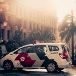 Viatura policial estacionada em área urbana, com palmeiras ao fundo.