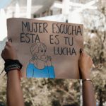 Participantes seguram cartaz em manifestação pelos direitos das mulheres ao ar livre.