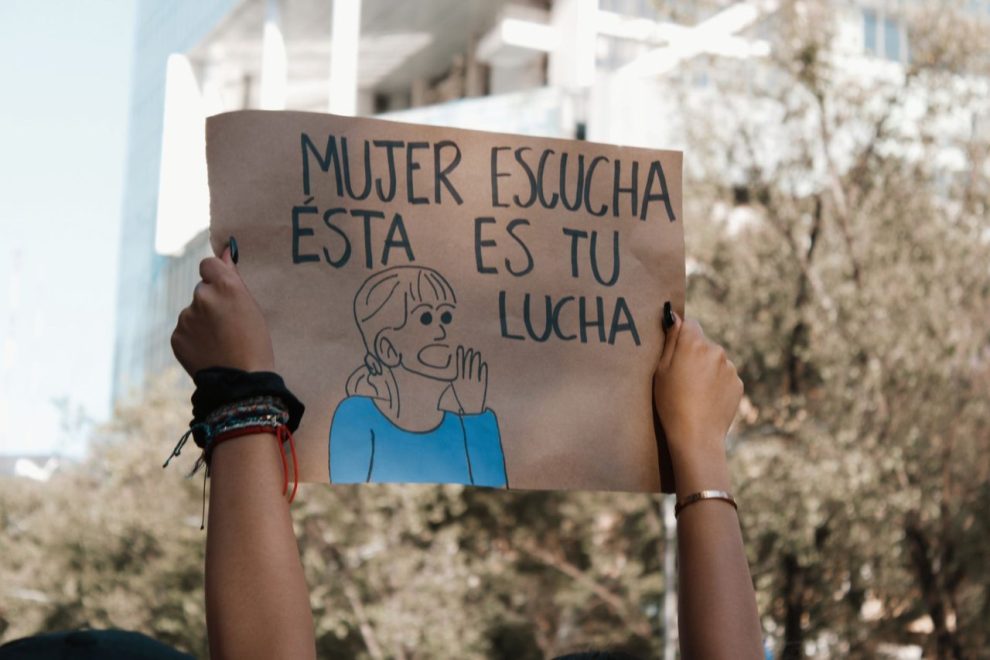 Participantes seguram cartaz em manifestação pelos direitos das mulheres ao ar livre.