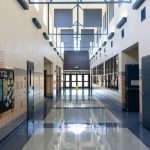 Corredor escolar vazio, bem iluminado e com arquitetura moderna, decorado com murais e quadros informativos.