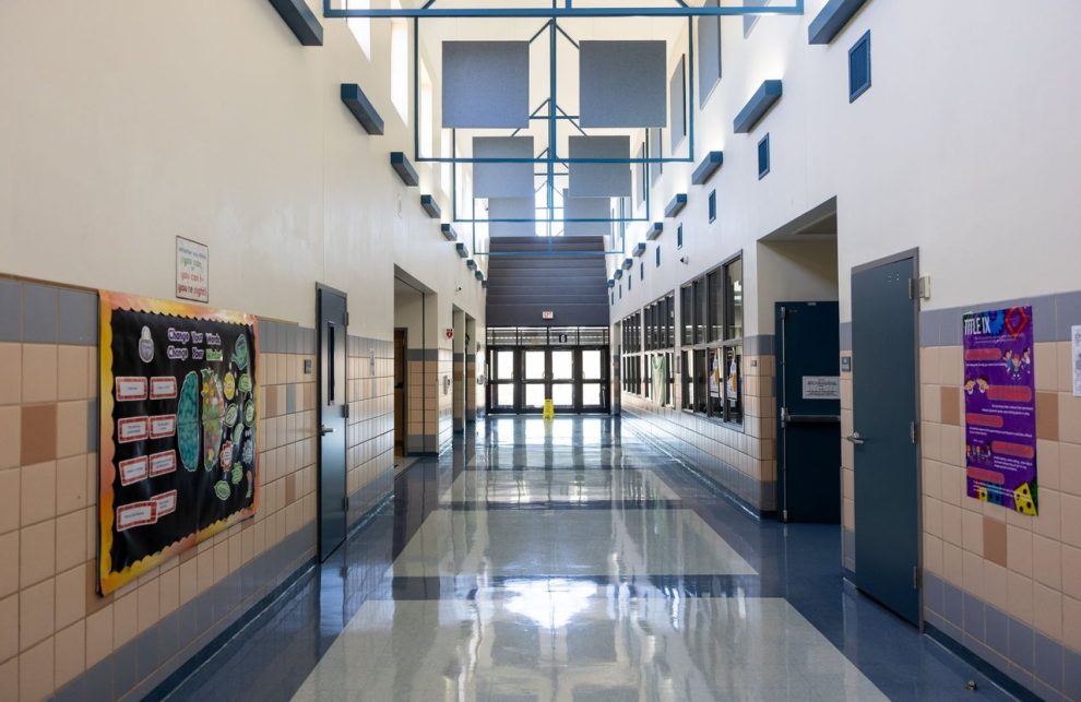 Corredor escolar vazio, bem iluminado e com arquitetura moderna, decorado com murais e quadros informativos.