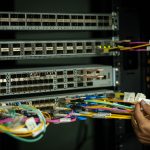 Mão de profissional organizando cabos de fibra óptica em uma sala de servidores.