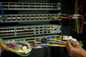 Mão de profissional organizando cabos de fibra óptica em uma sala de servidores.