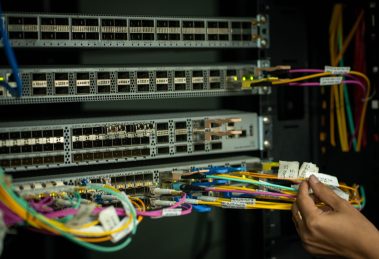 Mão de profissional organizando cabos de fibra óptica em uma sala de servidores.