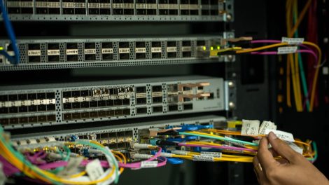 Mão de profissional organizando cabos de fibra óptica em uma sala de servidores.
