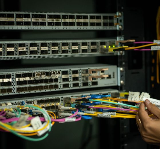 Mão de profissional organizando cabos de fibra óptica em uma sala de servidores.
