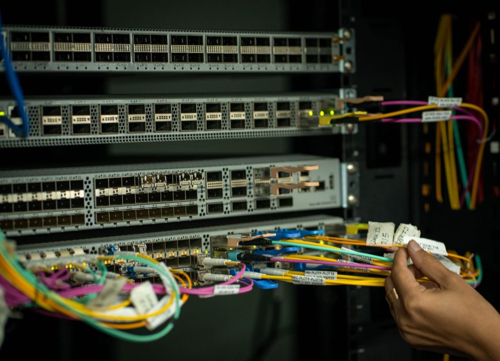 Mão de profissional organizando cabos de fibra óptica em uma sala de servidores.