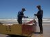 Dois pescadores preparam redes junto a um barco colorido na praia de Itaúnas, no Brasil.